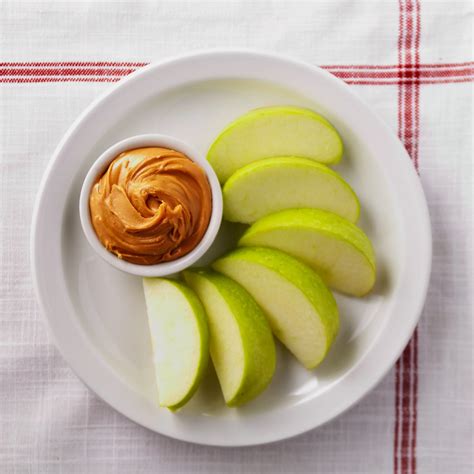 Apple slices with a small serving of peanut butter are arranged on a plate.