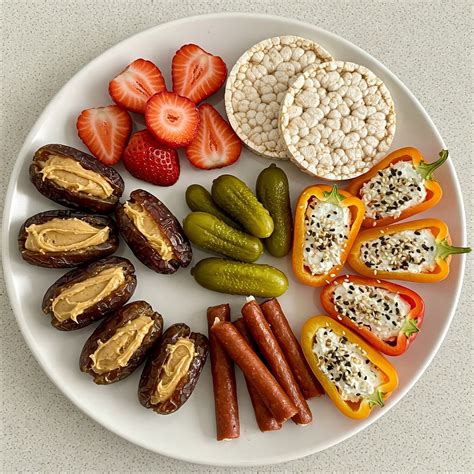 Greek yogurt, cottage cheese, hummus, berries, vegetables, crackers, and nuts are arranged on a kitchen counter.